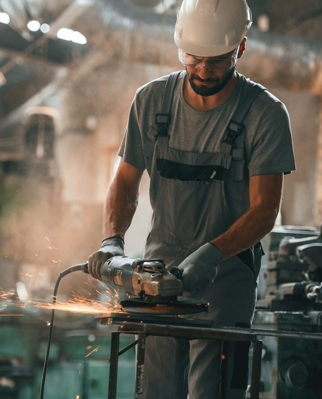 Angle grinder in hands. Young factory worker in grey uniform